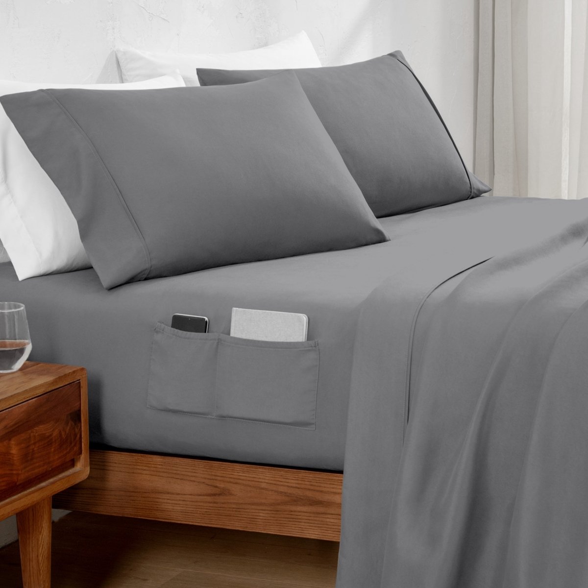 Gray bed sheets with pockets on a bed in a bedroom setting.