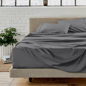 Gray sheet set on a bed in a room with a white brick wall and plants.