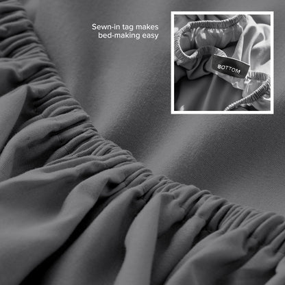 Gray fitted sheet with a sewn-in tag on a bed, showing close-up of the tag.