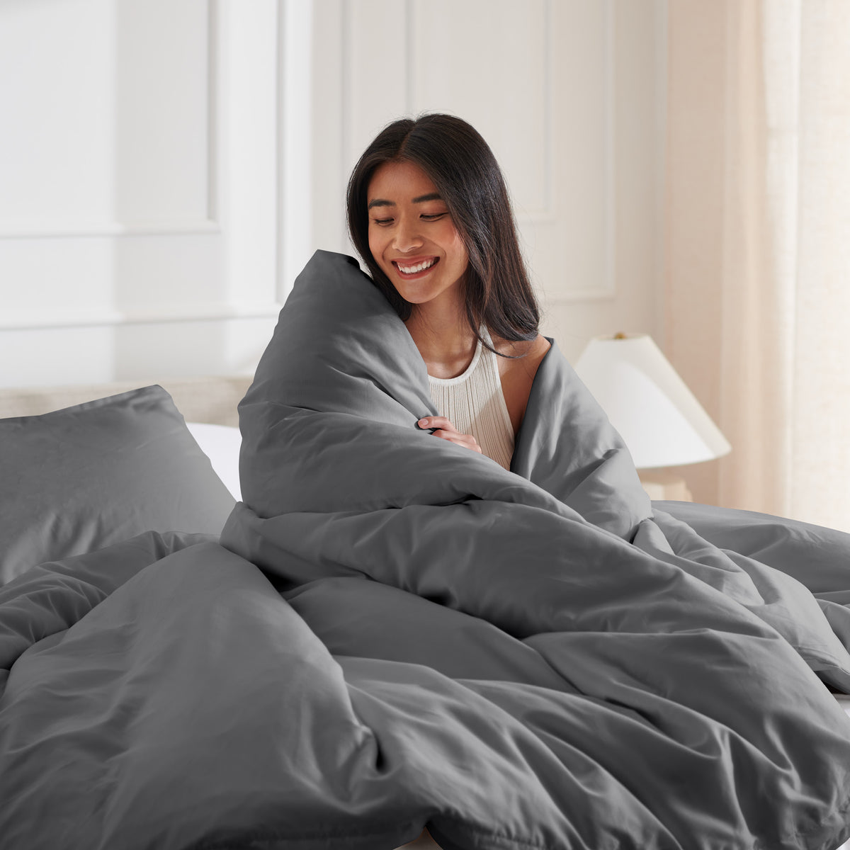 Woman smiling under duvet cover set in a bedroom setting