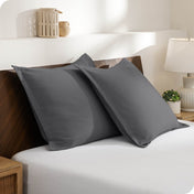 Two pillows with shams on a bed in a bedroom setting with a lamp and decor items.
