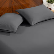 Fitted sheet and pillowcase set on a bed with a dark wood headboard and a small potted plant in the background.