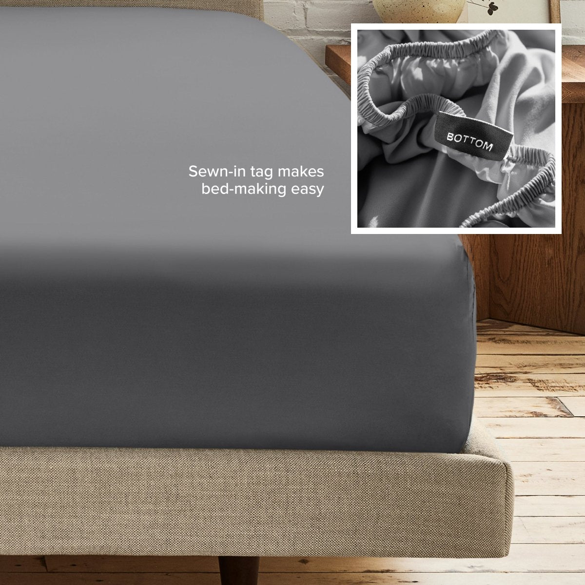 A fitted bed sheet on a bed frame with a small inset close-up of the elastic and a sewn-in tag labeled BOTTOM. White text on the sheet reads, 'Sewn-in tag makes bed-making easy.