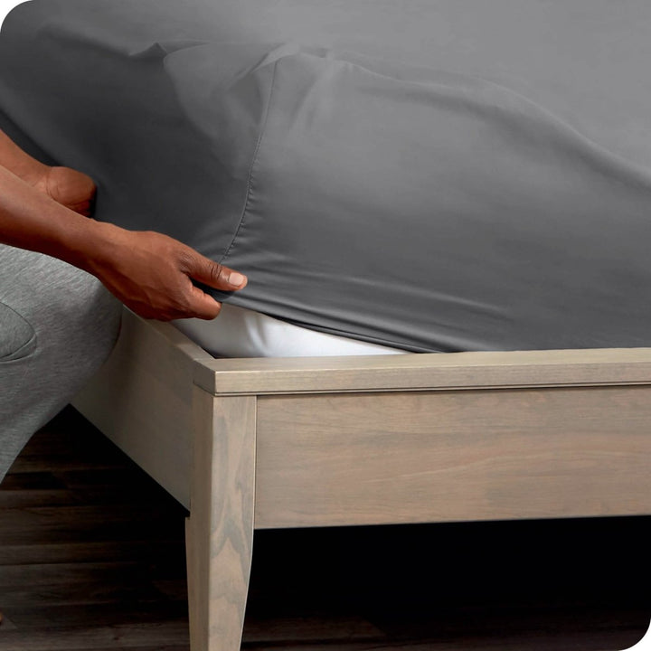 A man is kneeling while putting a fitted sheet on a mattress