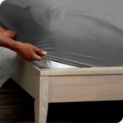 A man is putting a fitted sheet on a mattress