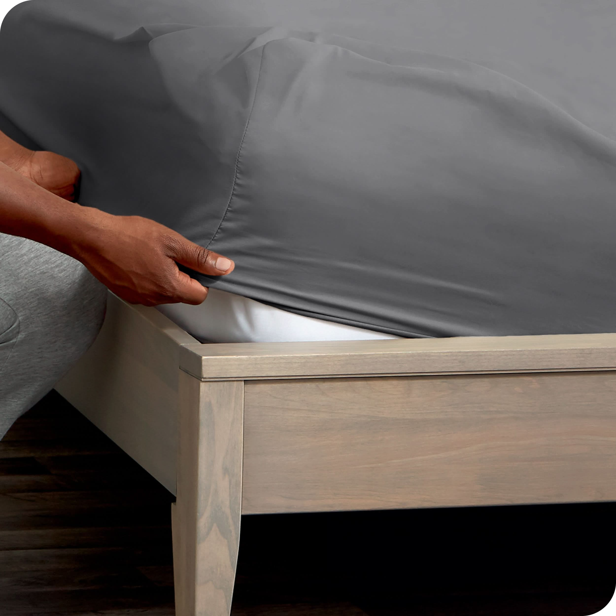 A man is putting a fitted sheet on a mattress