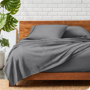 A wooden bed frame with a microfiber sheet set on the mattress.