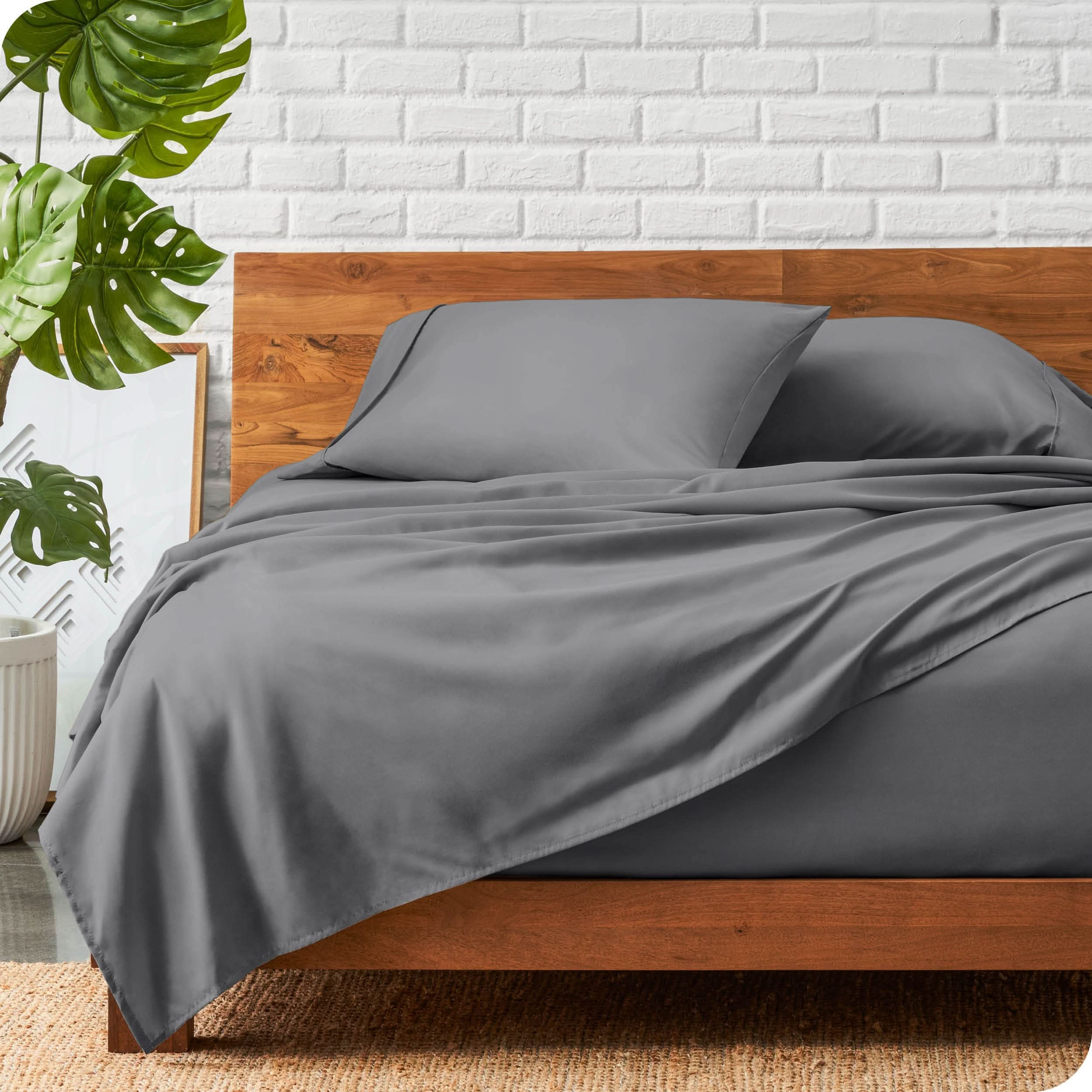 A wooden bed frame with a microfiber sheet set on the mattress.