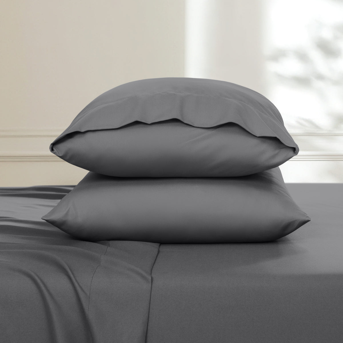 Two pillows stacked on a bed with a neutral background