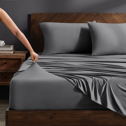 Person adjusting stretch sheets on a bed with a wooden headboard.