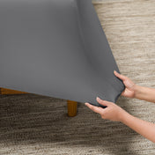 Person putting a fitted sheet on a bed on carpeted floor.
