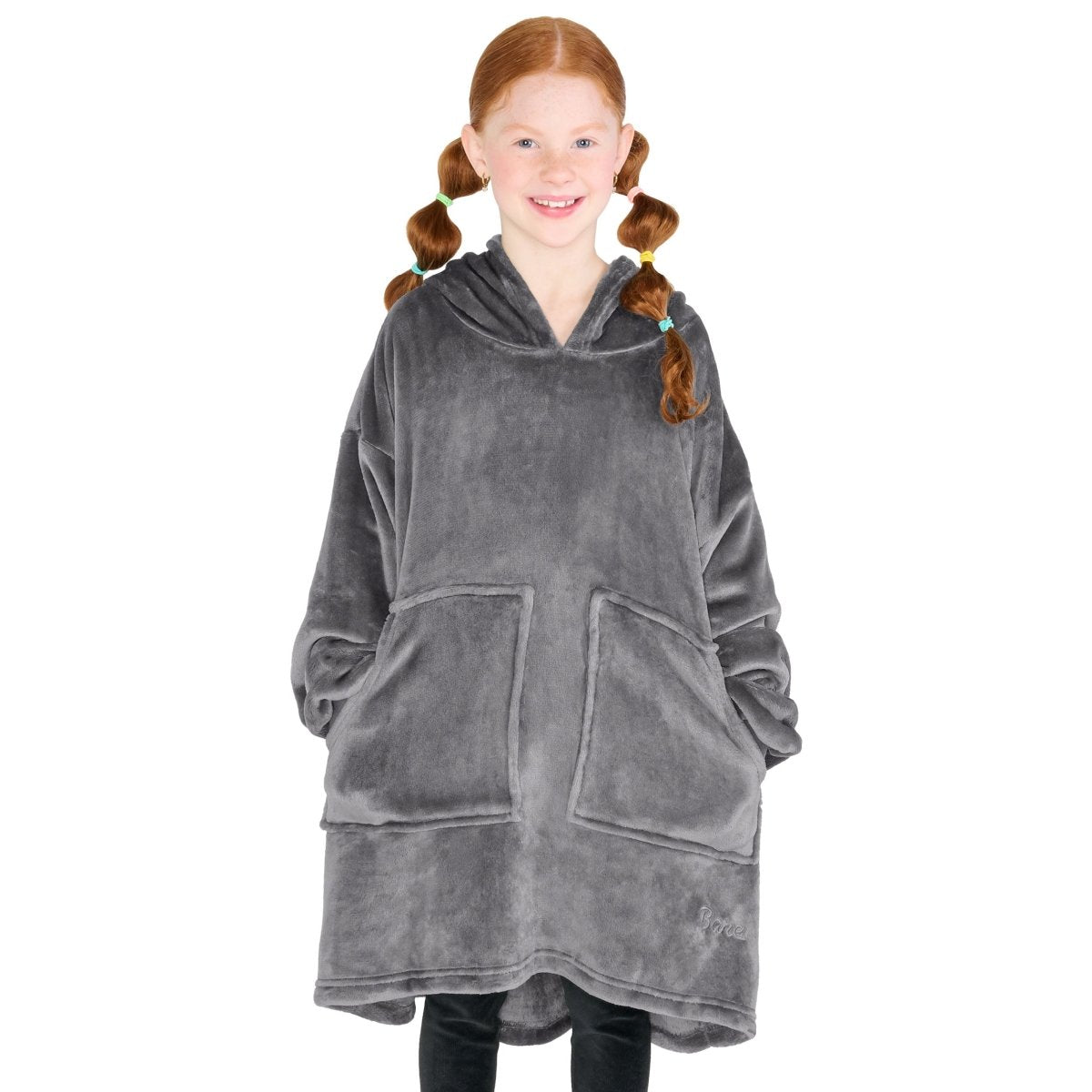 A girl is standing while wearing a microplush wearable blanket with her hands in the pockets