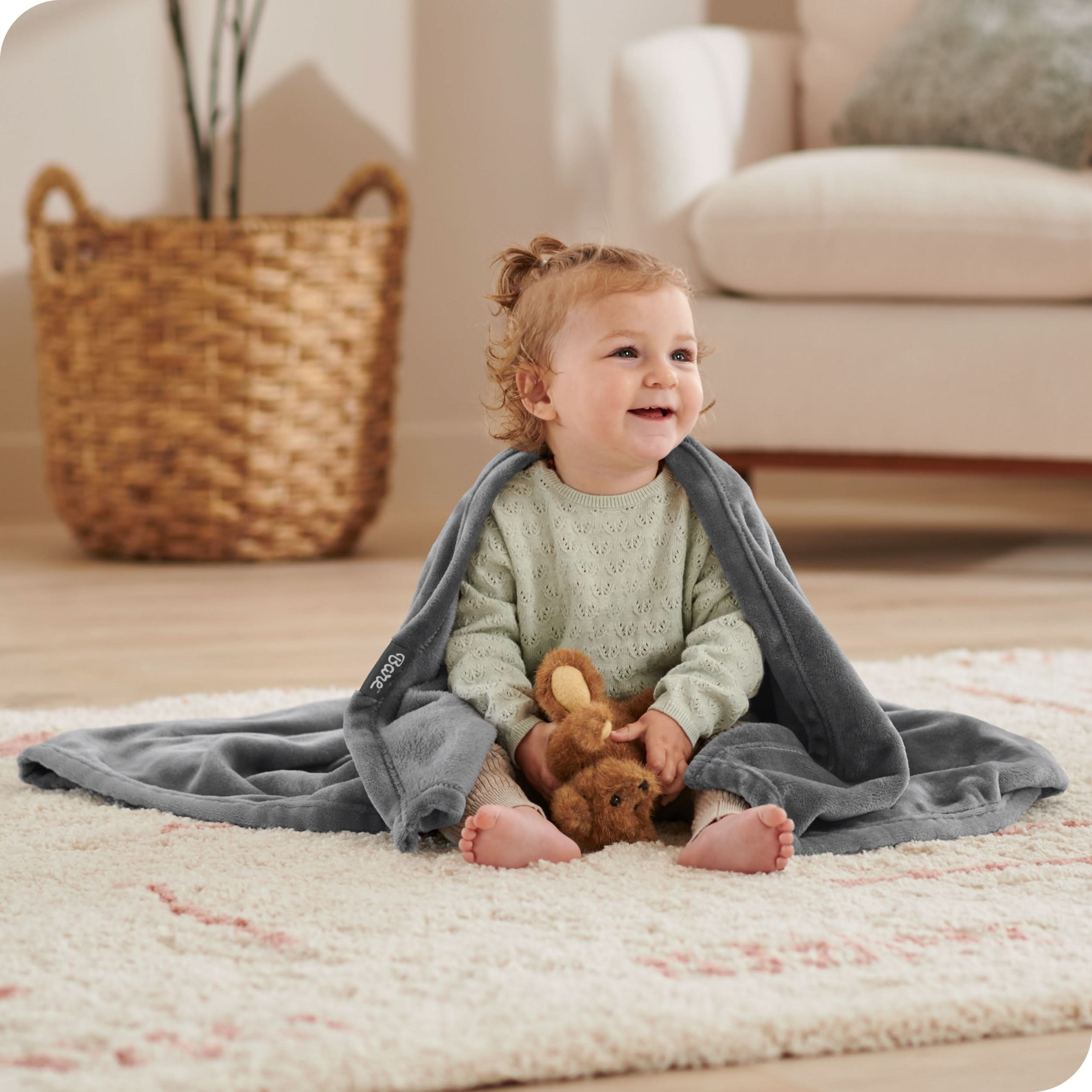 A baby sitting on the floor with a blanket around her shoulders