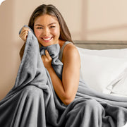Woman sitting on a bed cuddling with a microplush blanket