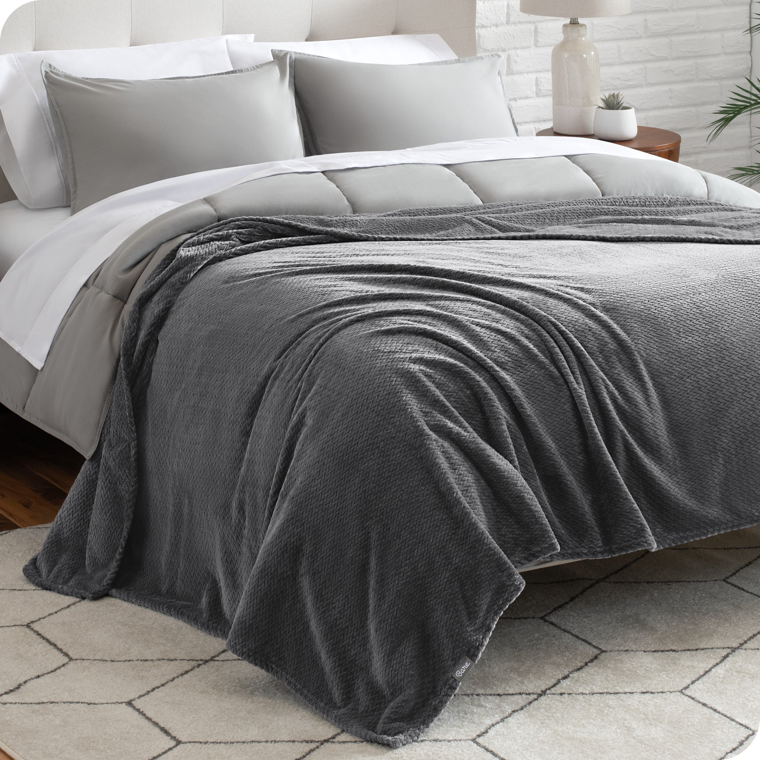 A textured microplush blanket is covering a bed, which has a comforter set on it.