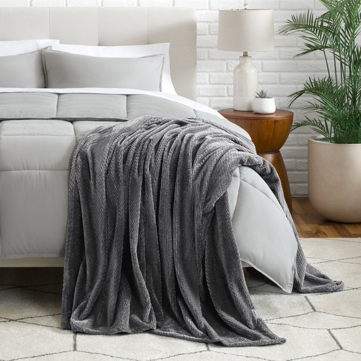Blanket draped over a bed in a bedroom setting with a lamp and plant.