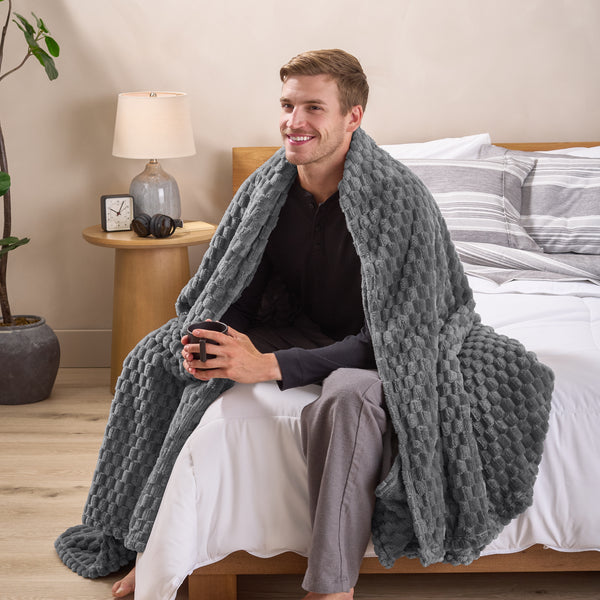 A man sitting on a bed wrapped in a microplush blanket