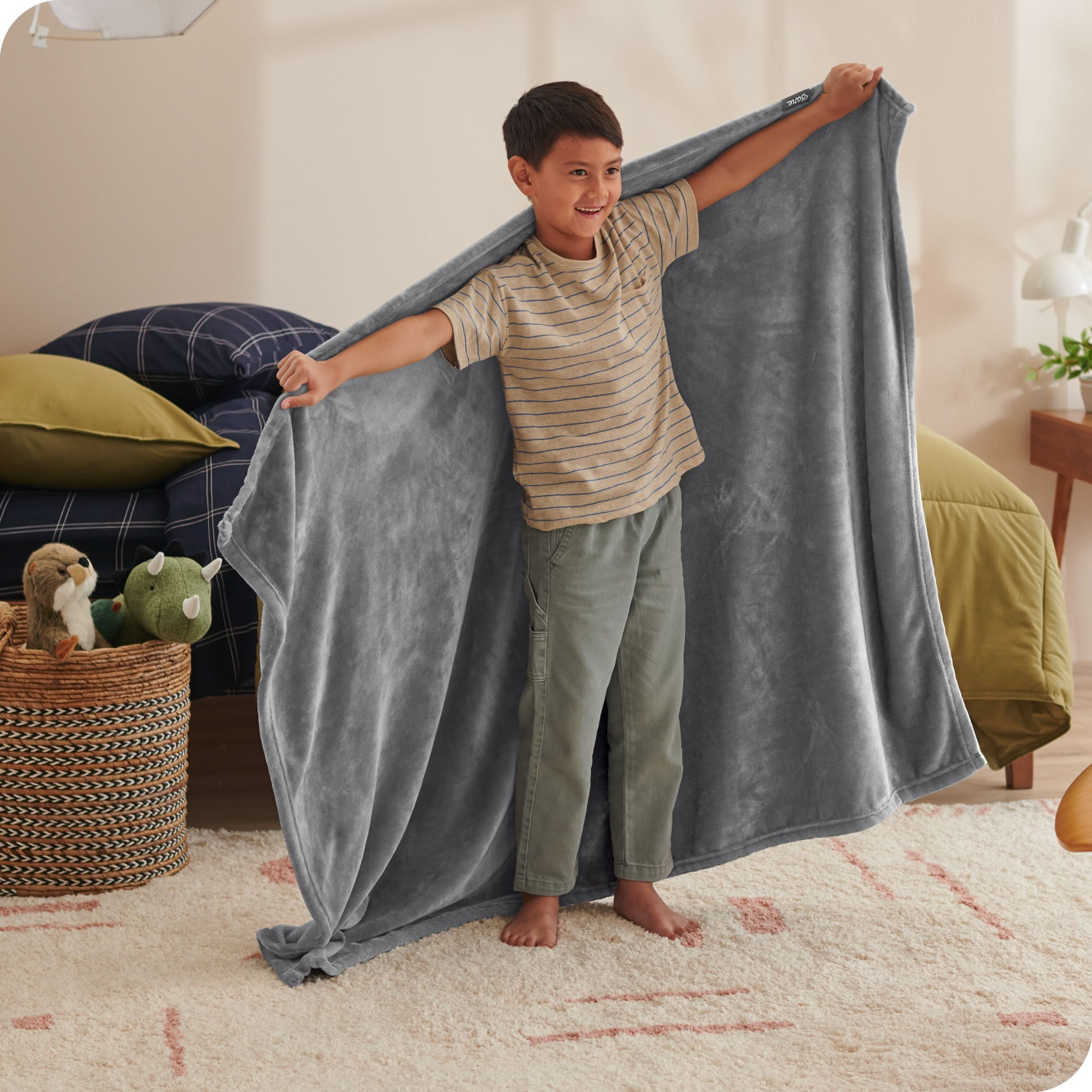 A child has his arms stretched out while holding a microplush blanket behind him