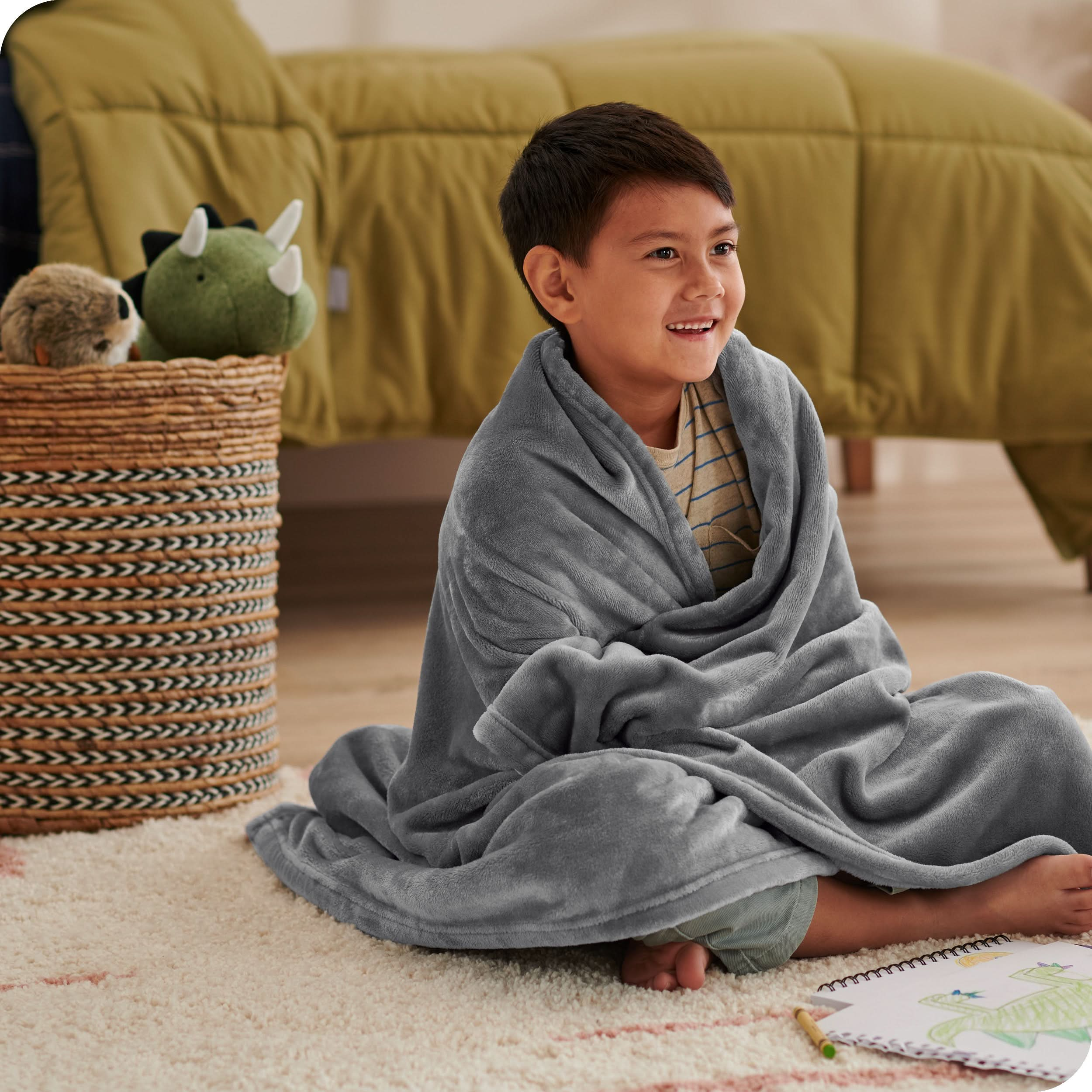 A boy is sitting on the floor of his bedroom with a microplush blanket wrapped around him