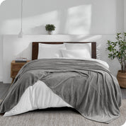 An oversized blanket on a bed made with all white bedding