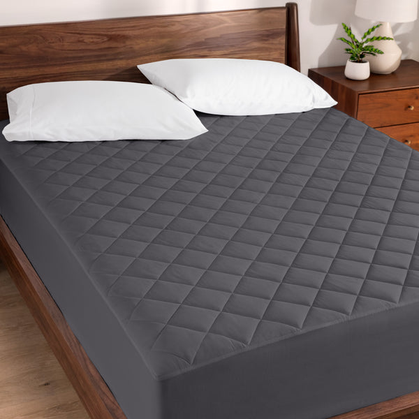 Quilted mattress pad on a bed with wooden headboard and nightstand.