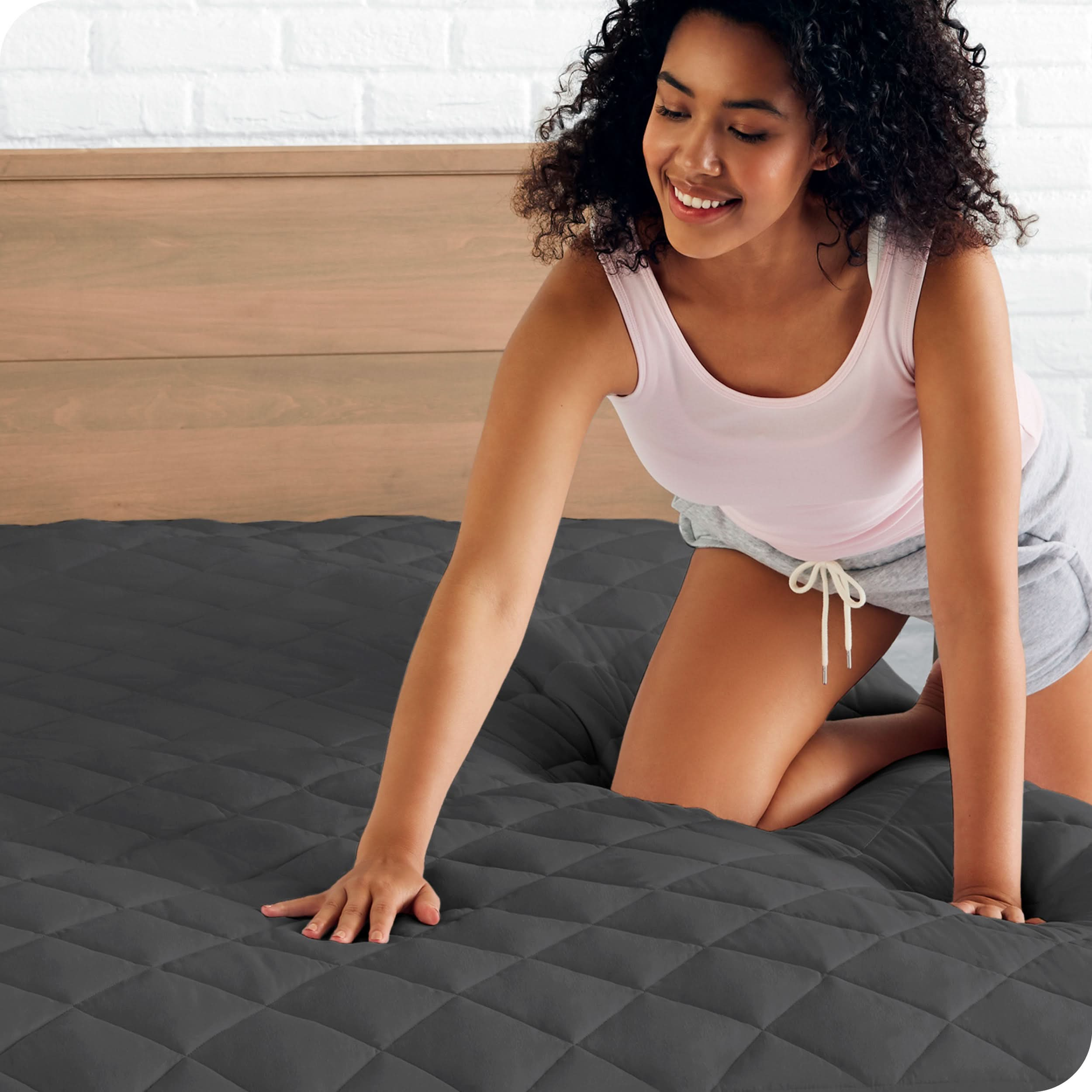 A woman is pressing her hand on a mattress with a quilted mattress pad on it