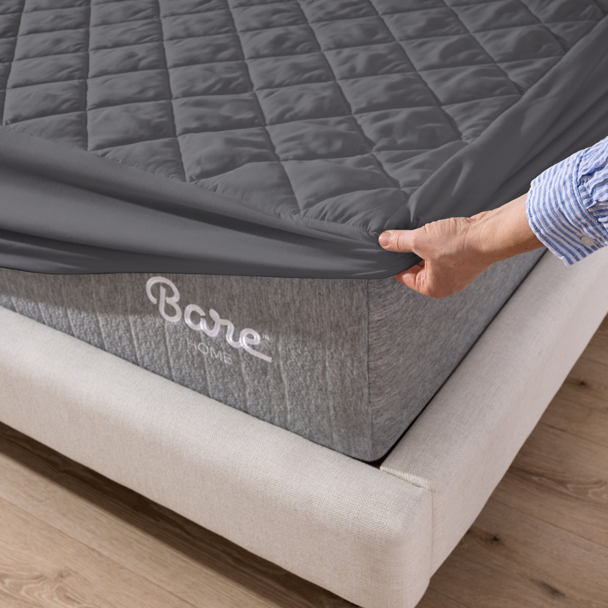 Person putting a mattress cover over a Bare Home branded mattress on a wooden floor.