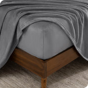 The corner of a bed frame and mattress with a fitted sheet and flat sheet on it.