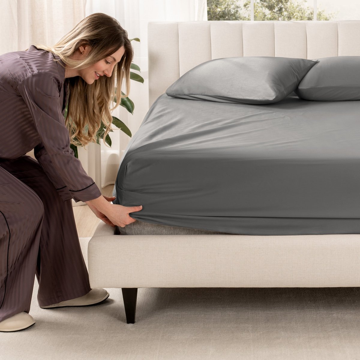 Woman adjusting a fitted sheet on a bed in a bedroom setting