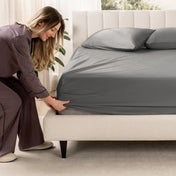 Woman adjusting a fitted sheet on a bed in a bedroom setting