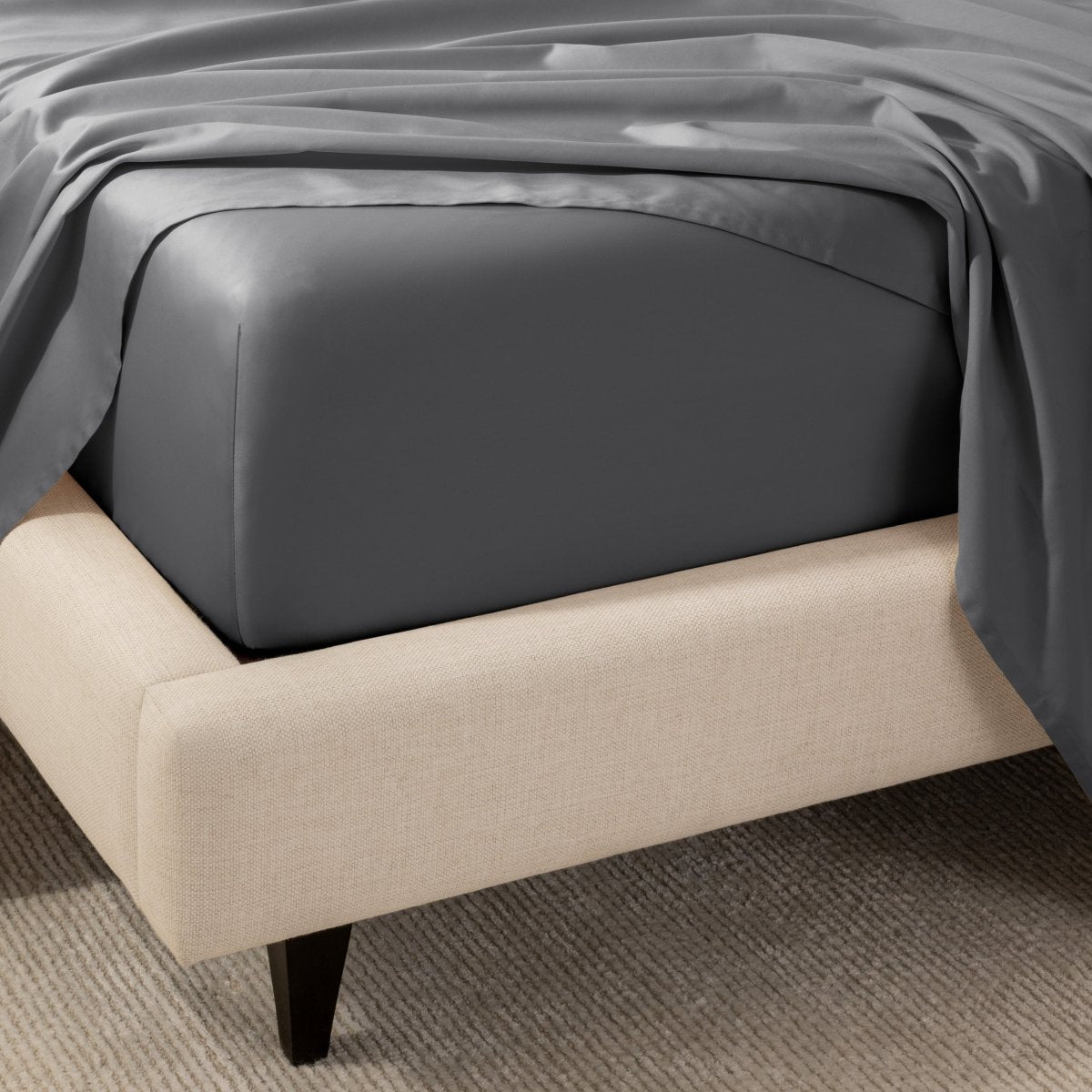 A close-up of the corner of a bed with a fitted sheet and matching flat sheet.