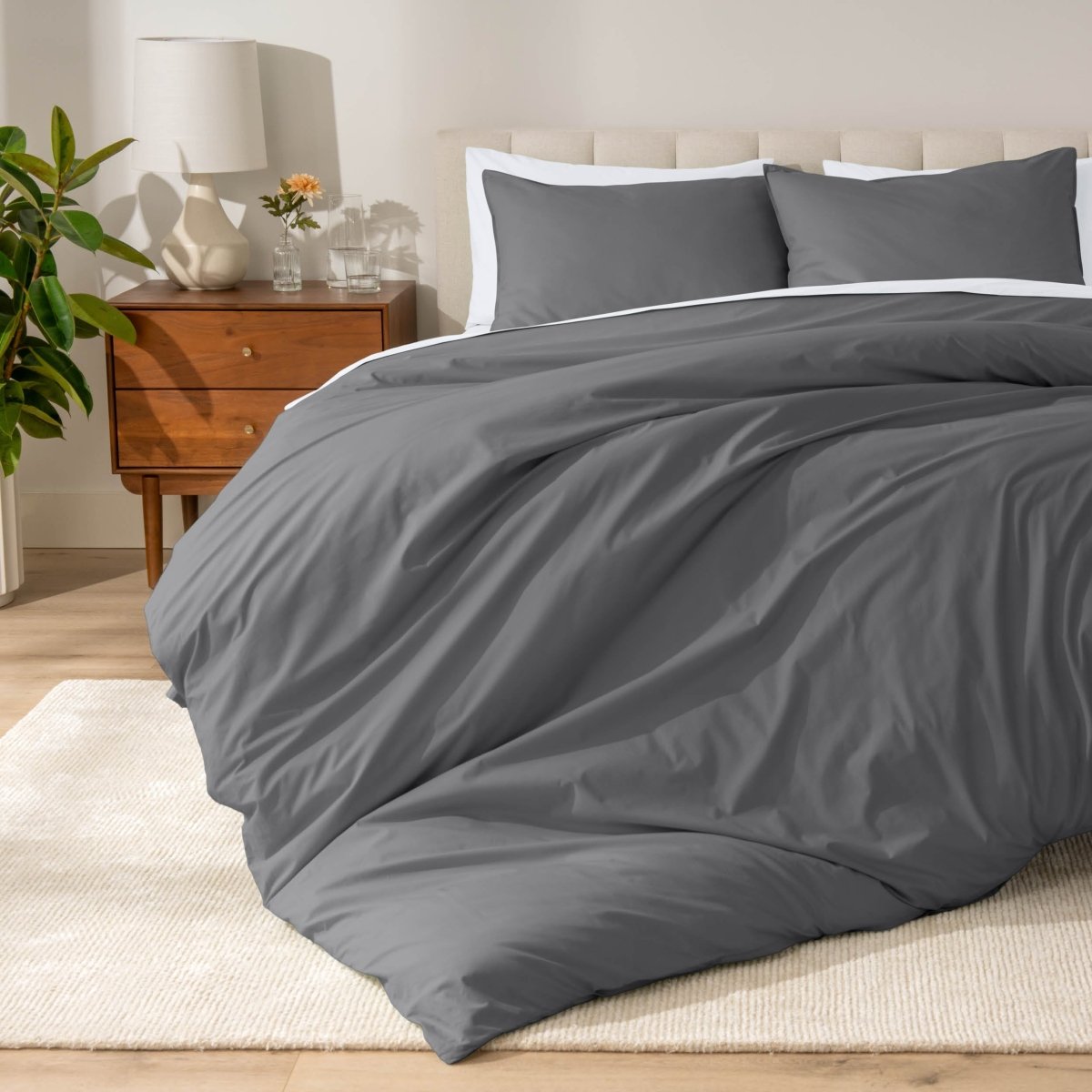 Percale bedding set on a bed in a bedroom with a wooden nightstand and lamp.