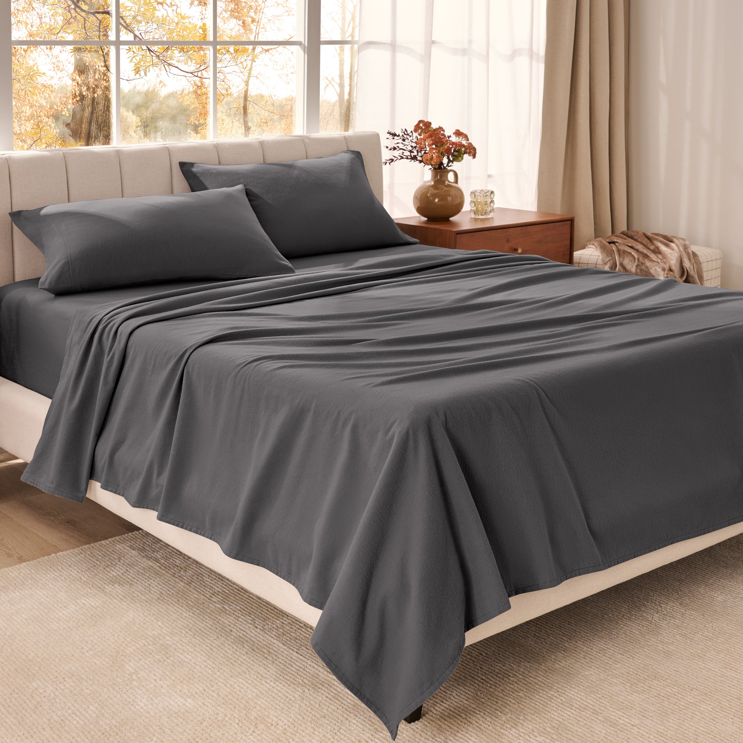 Bed sheets on a neatly made bed in a bright bedroom with large windows.