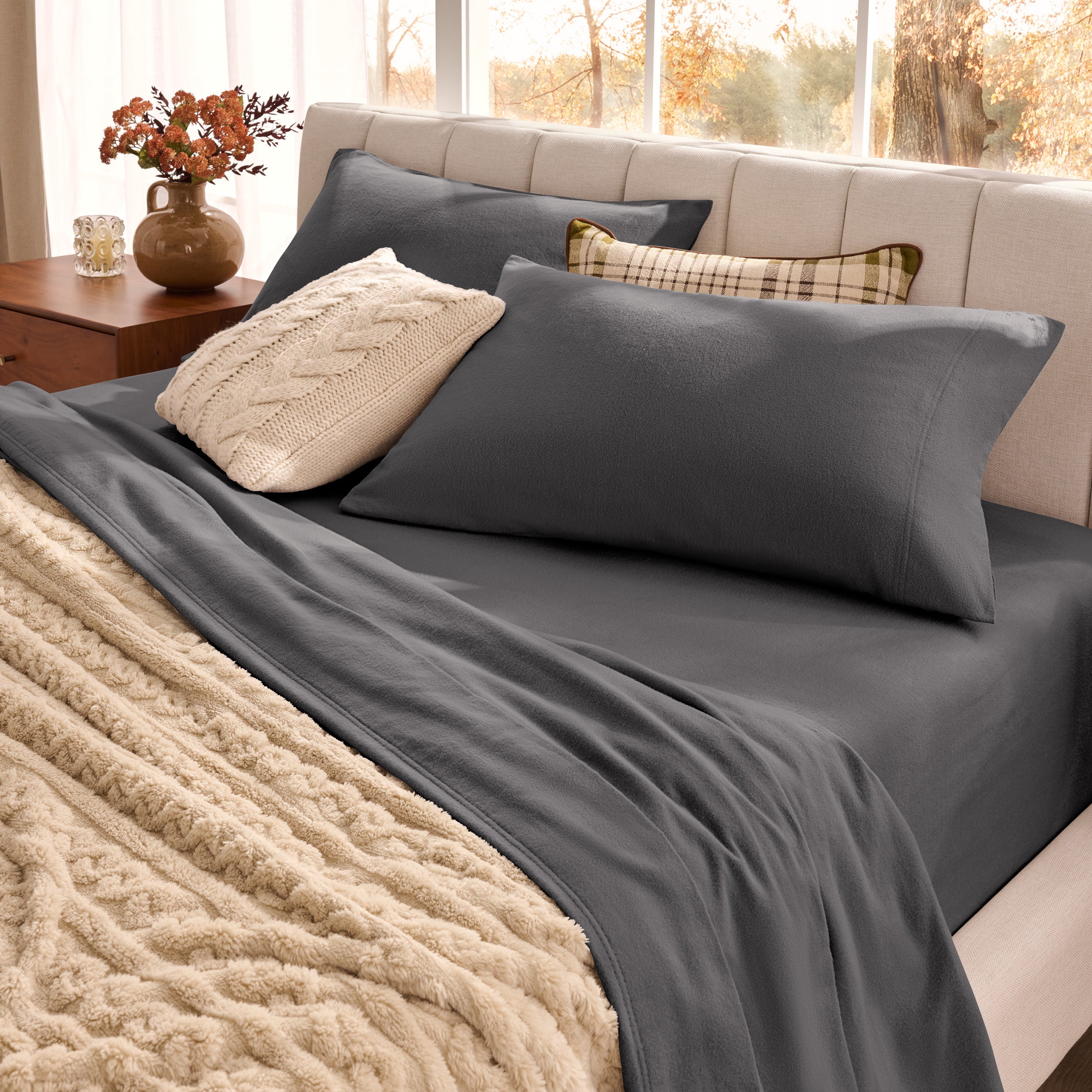 Neatly made bed with organic flannel sheets  and a beige blanket in a bright bedroom.