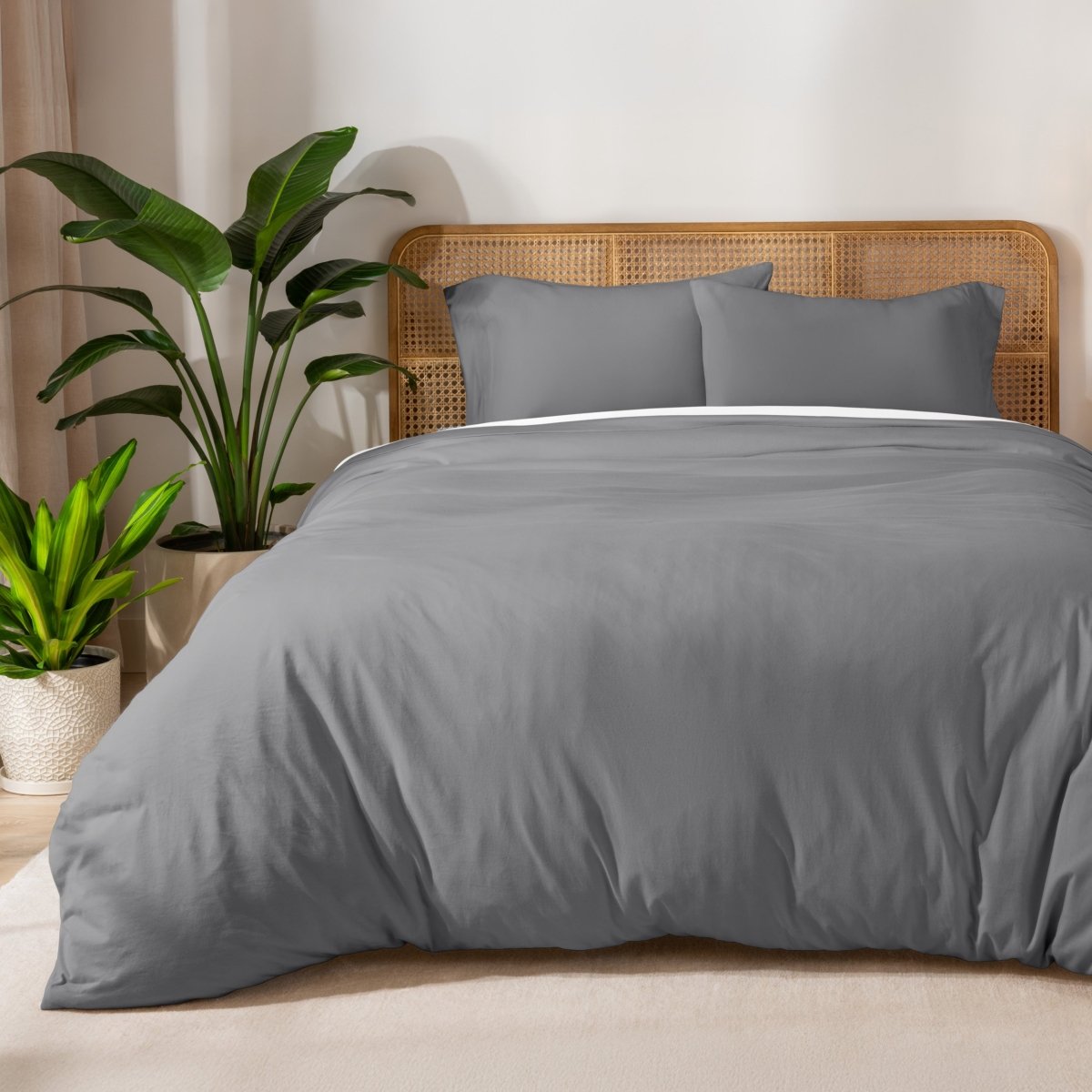 Gray duvet set on a bed with a wicker headboard and plants in the background.