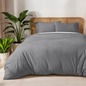 Gray duvet set on a bed with a wicker headboard and plants in the background.