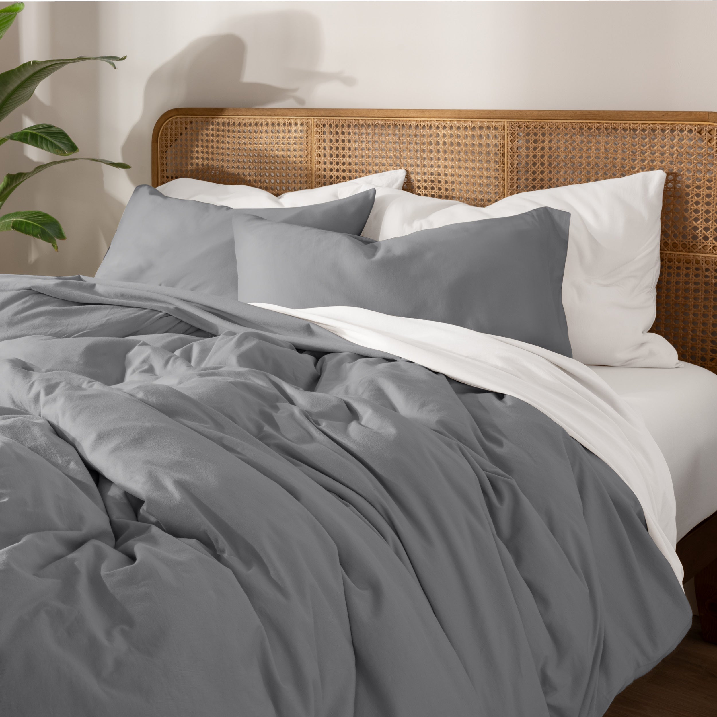 A neatly made bed with gray bedding, white pillows, and a wooden headboard. 