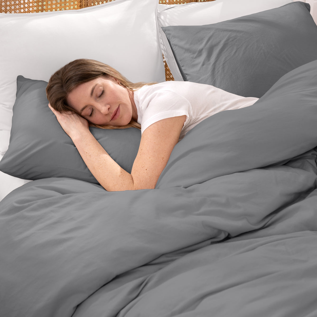 Woman sleeping under gray bedding with white pillows