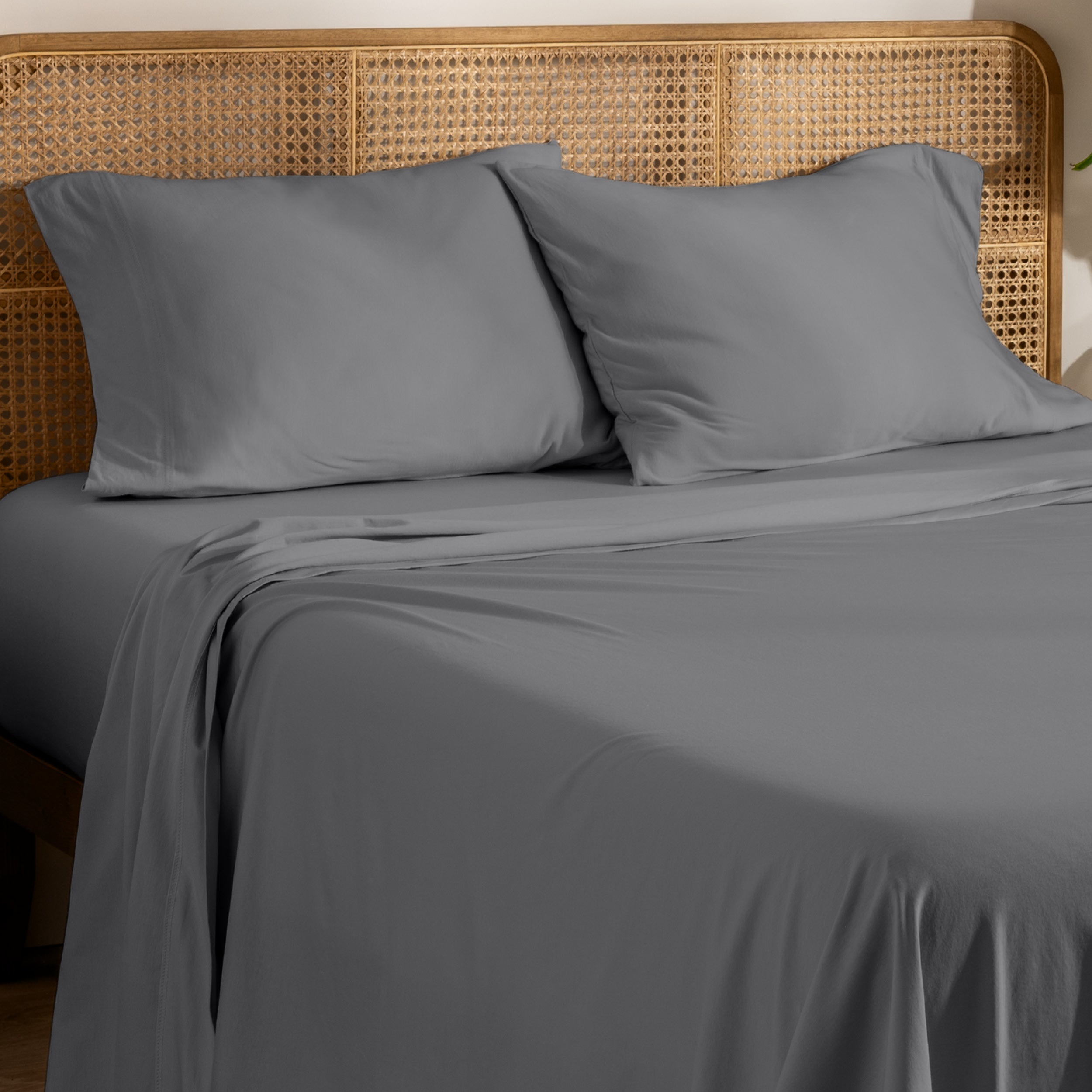 Organic jersey bed sheets and pillows on a bed with a wicker headboard.