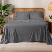 Organic cotton jersey sheets on a bed with a wicker headboard in a room with plants and a lamp.