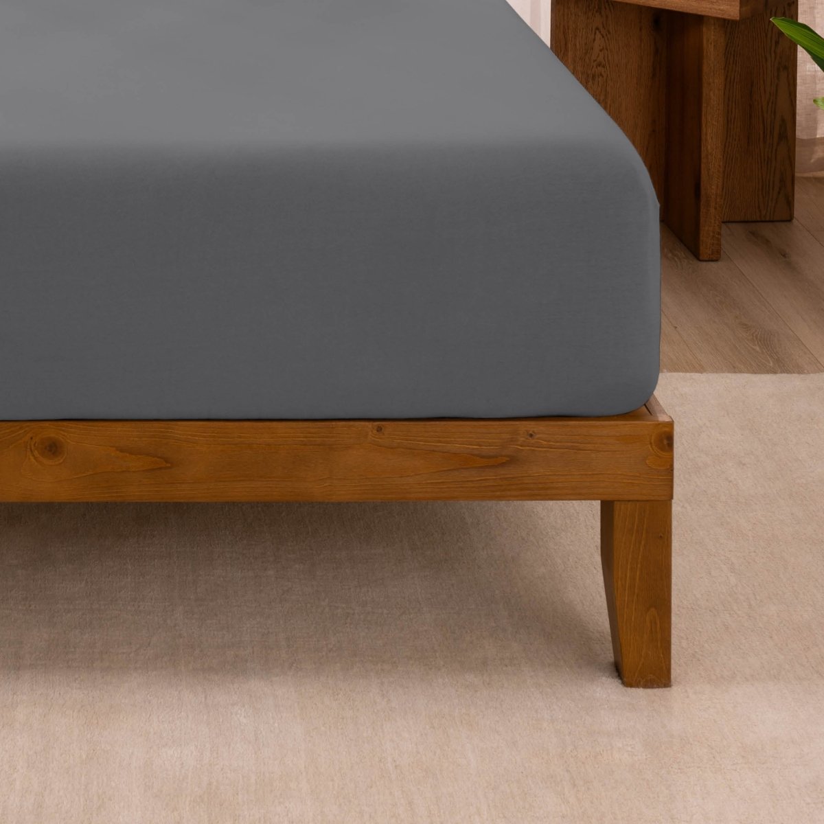 Fitted sheet on a wooden bed frame with a neutral background