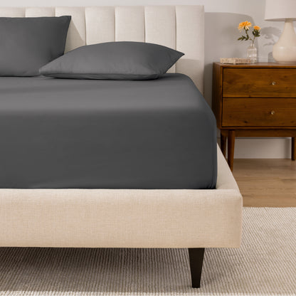 A percale fitted sheet and pillowcases on a bed in a bedroom with a wooden nightstand.