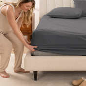 Woman in pajamas adjusting bed sheets on a bed.