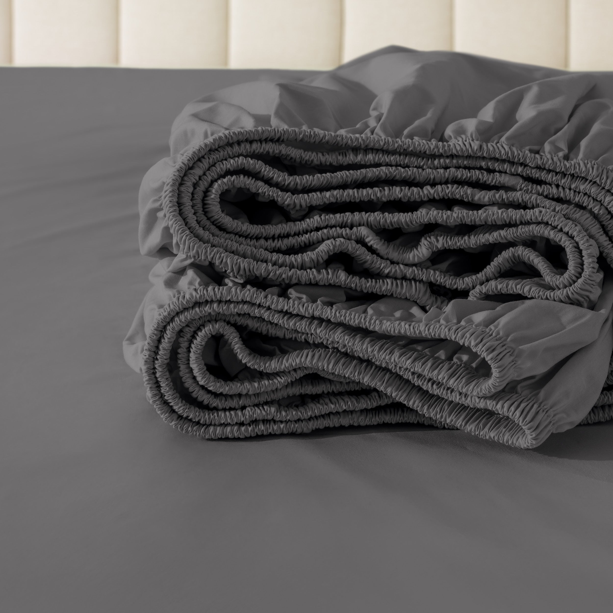 Folded fitted sheet on a bed with a neutral background