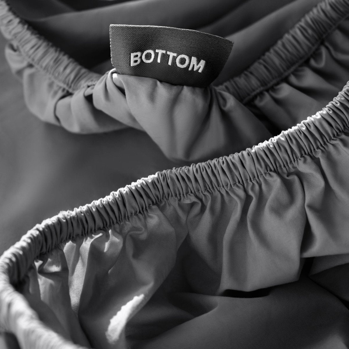 Close-up of a fitted sheet with a black fabric brand label reading BOTTOM.