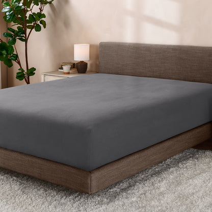 Bed with fitted sheet in a room with a lamp and plant.