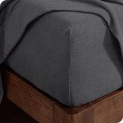 Corner of the bed with a fitted sheet on the mattress and a flat sheet draped over the side and end