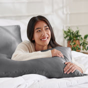 Woman lying on a bed with a body pillow, smiling.