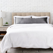 Bed with white bedding and a gray pillow against a white brick wall.