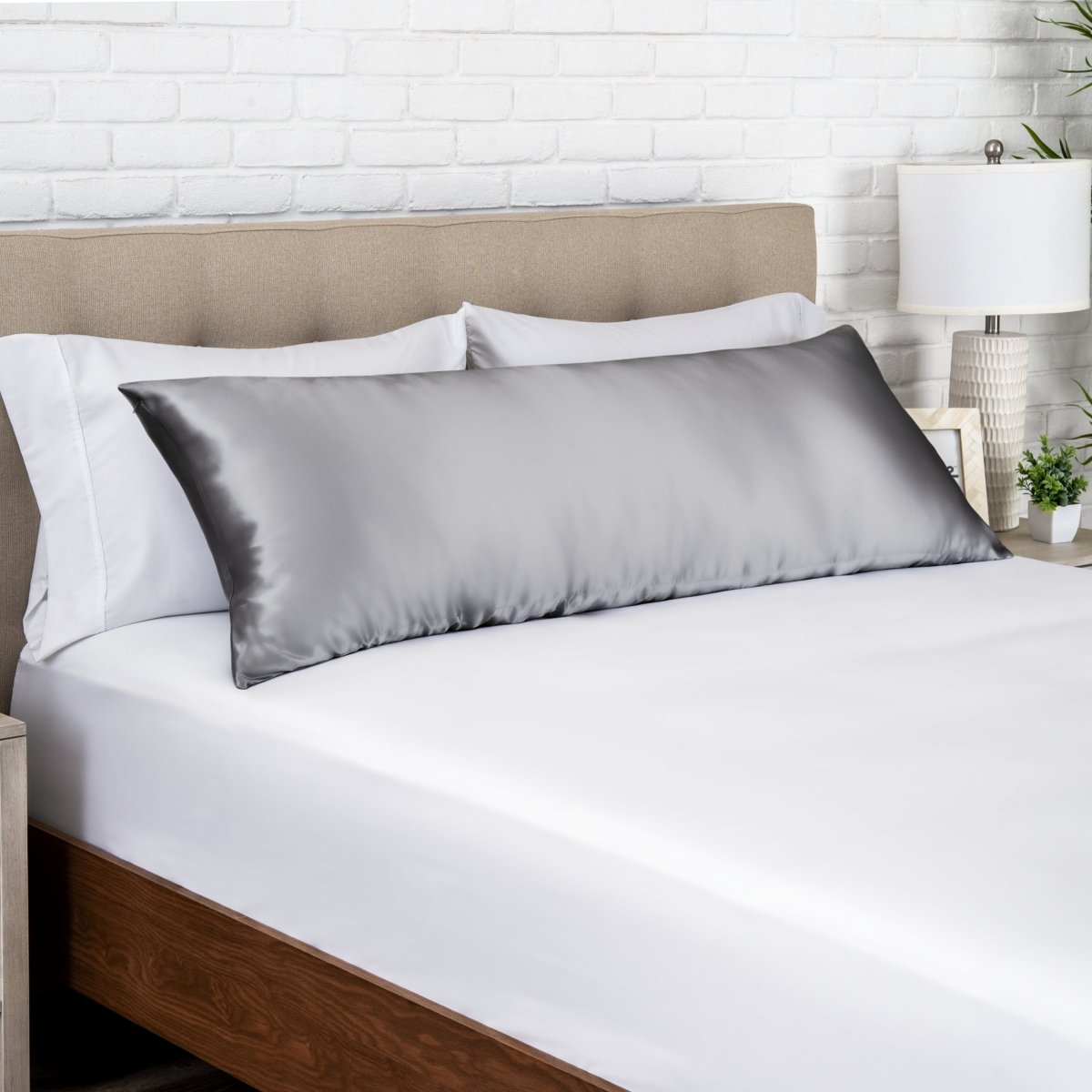 Gray satin pillow on a bed with white bedding and a wooden headboard.
